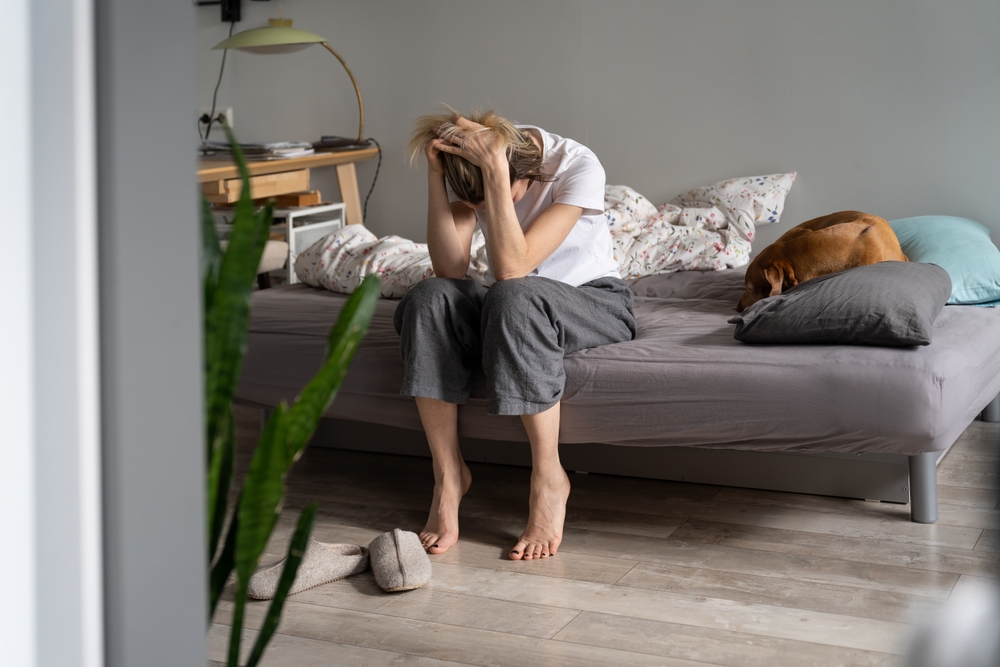 midlife woman upset sitting on bed at home, holding head in hands