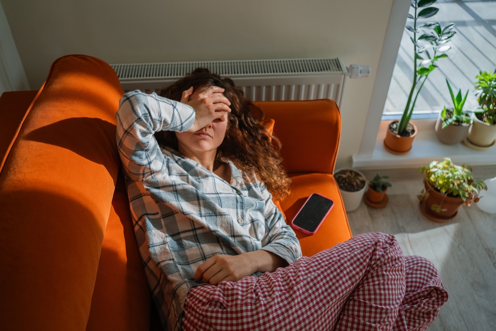 woman feeling sick and exhausted lying on sofa, signs of nervous system dysregulation