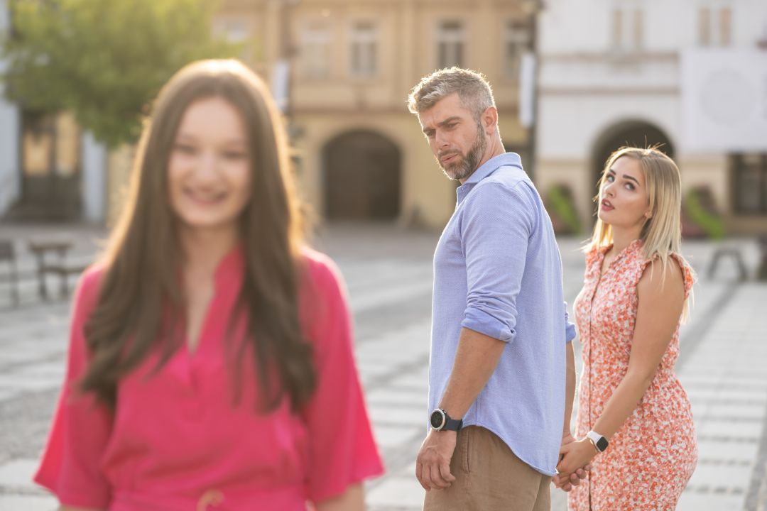 Disloyal man walking with his girlfriend and looking amazed at another seductive girl