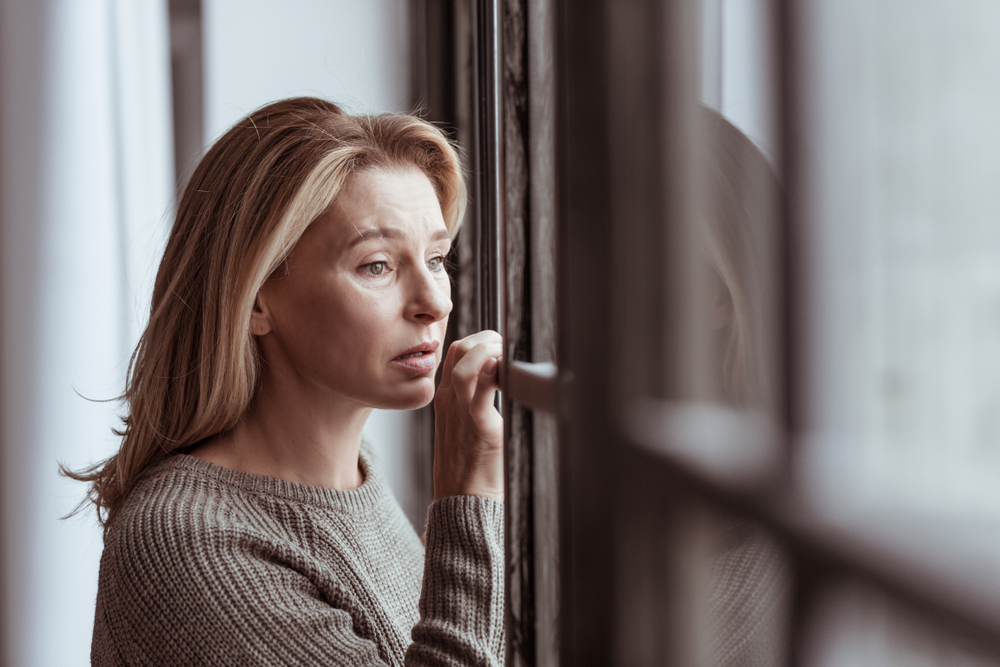 midlife woman looking out of window feeling fear, dread and worry because of hormonal changes during menopause