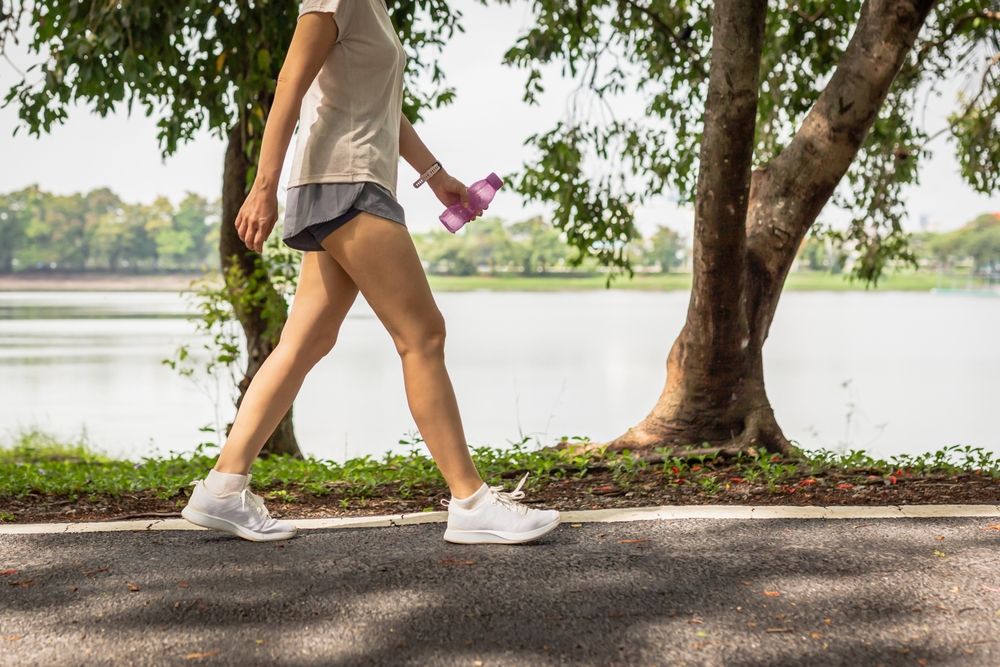 a woman holding a water bottle in athletic gear, walking outdoors for fitness