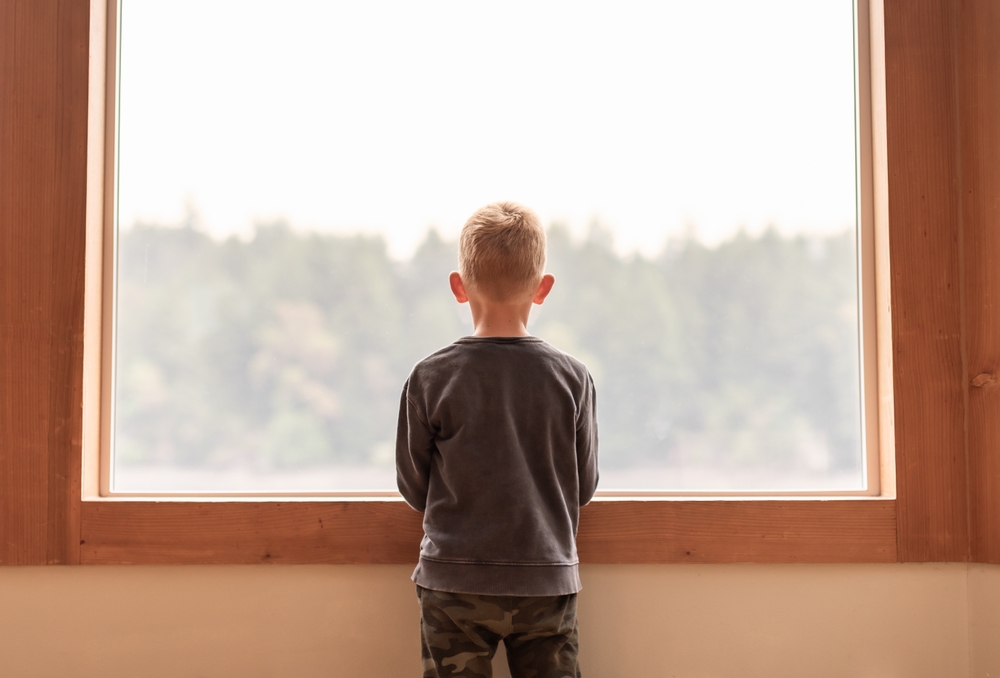 child looking out of window at home alone