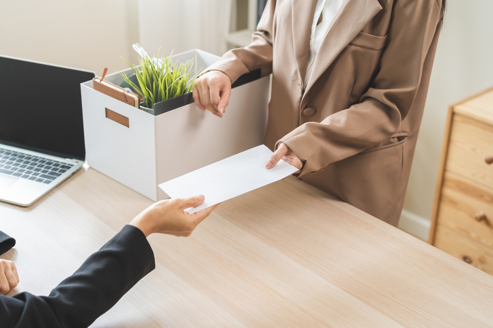 woman resigning from her job, handing a letter to her boss and packing up her desk