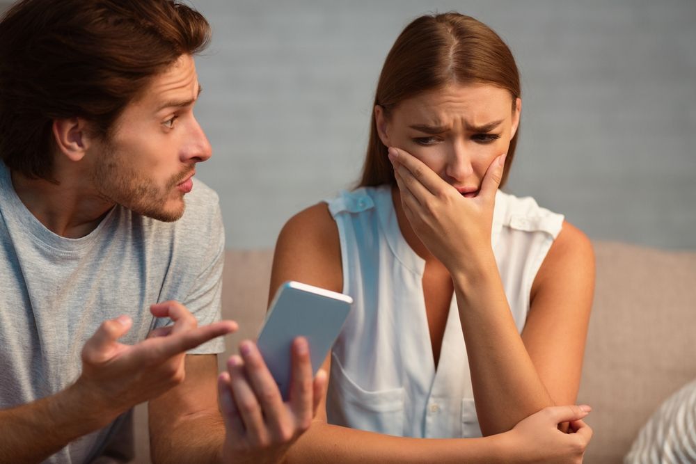 Woman looking upset while her partner holds a phone, looking for answers