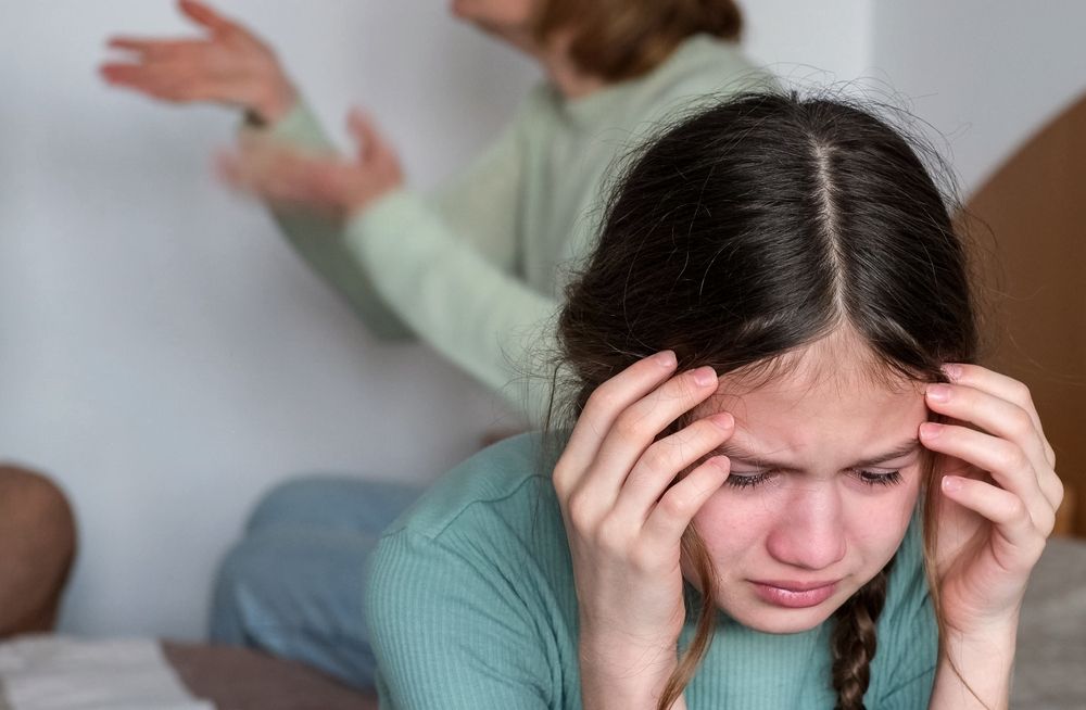 A child with braids looking upset while parents argue in the background