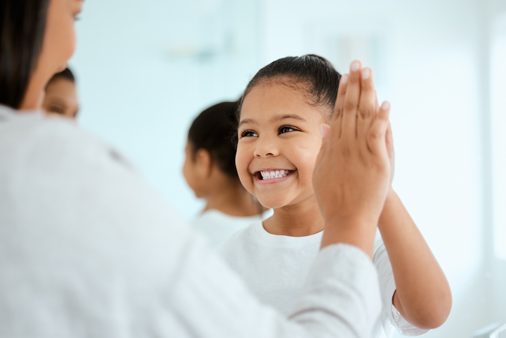 young girl being praised by her parent, high fiving and smiling