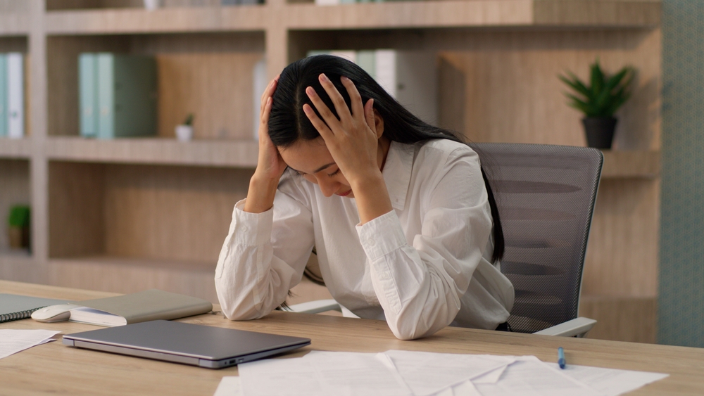 woman at desk with head in her hands, feeling tired, bored unfocused