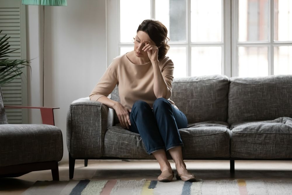 middle aged midlife woman crying while sitting on the sofa, experiencing menopause hormonal changes