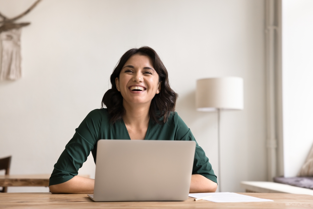 woman sitting at desk with laptop out smiling feeling happy and hopeful about the future