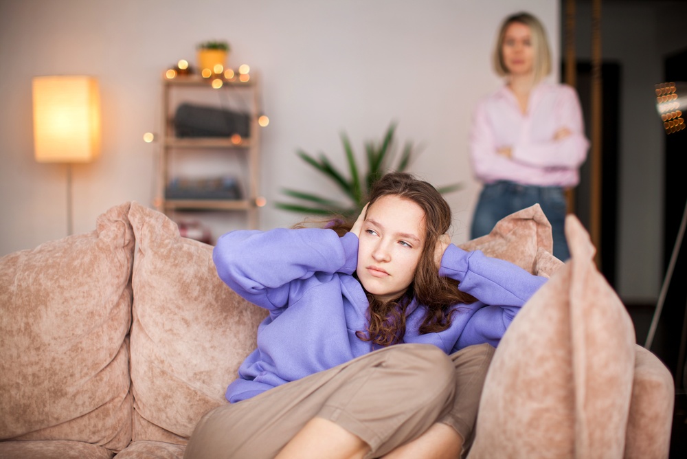 teenage daughter holding her hands over her ears, she is in an argument with her mum