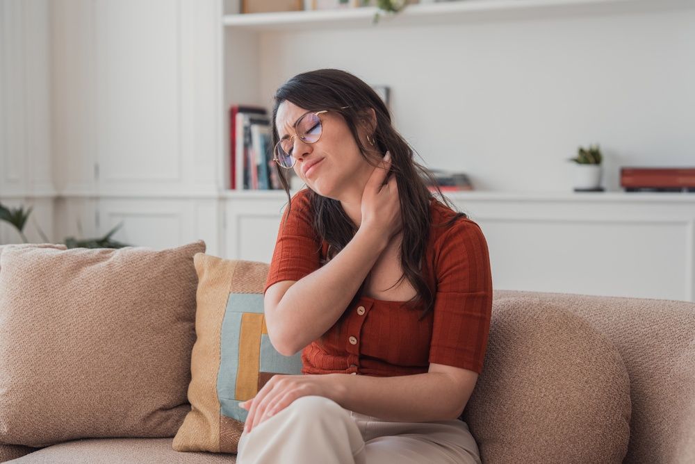woman with neck pain sitting on sofa massaging muscles and fascia