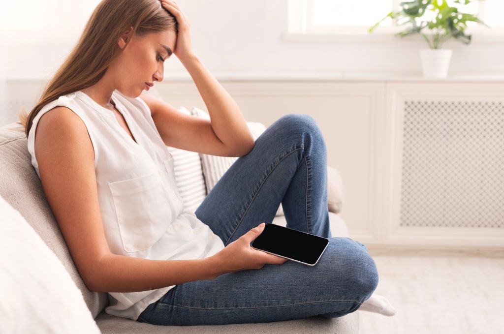 A woman looking sad and disappointed as she looks at her phone