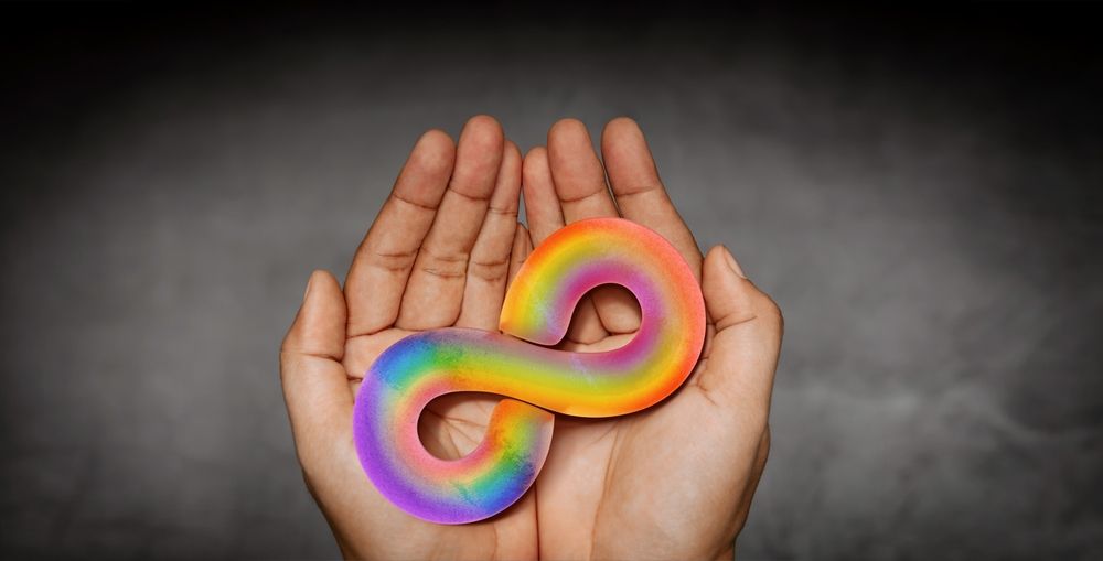 Hands holding a rainbow-coloured infinity symbol, the symbol for autism
